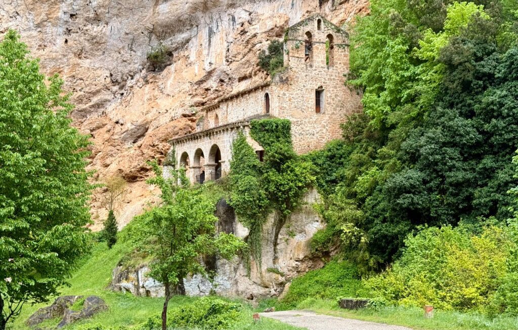 Explore the historic monastery nestled within a lush, green Spanish cliffside setting.