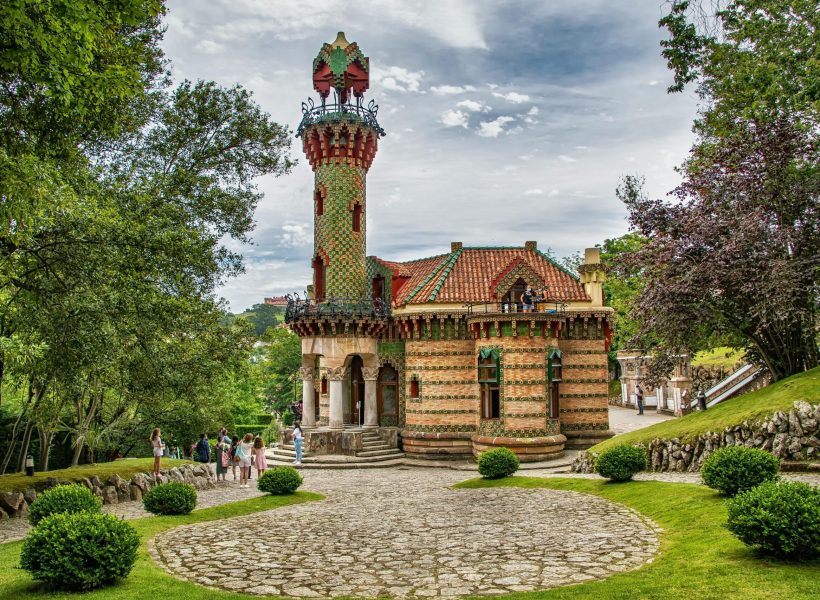 Ornate building surrounded by lush gardens and trees in Comillas, Spain.